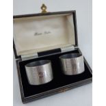 A pair of cased silver napkin rings, London 1963, with engine turned design and catouches to front