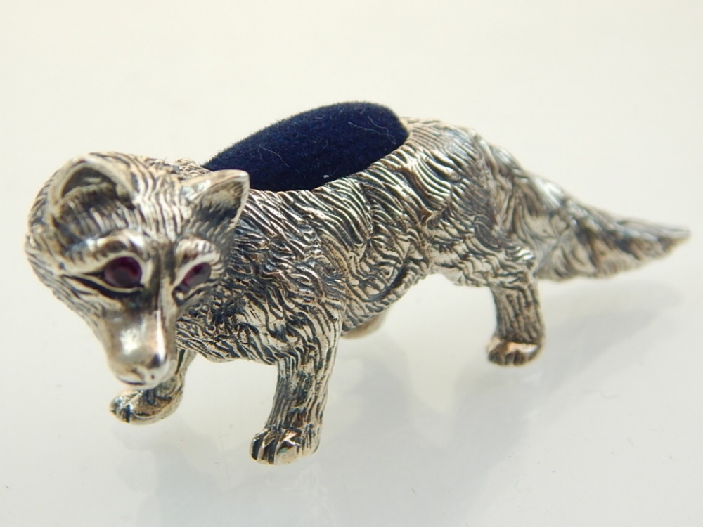 A white metal pin cushion modelled in the form of a fox, with ruby eyes.