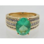 An emerald and diamond dress ring, the central oval cut stone flanked by three rows of diamond to