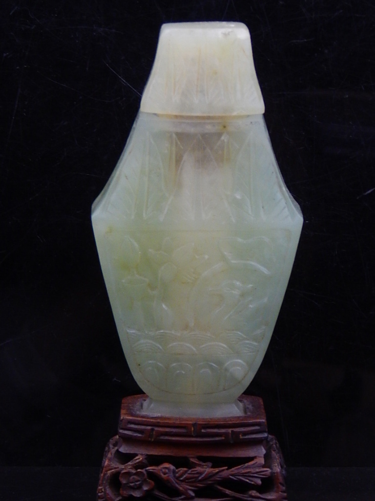 A Chinese green hardstone snuff bottle, raised on a hardwood stand, H.16cm.