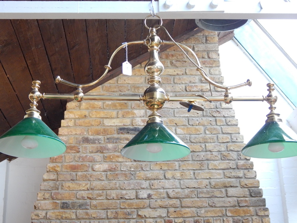 A tubular brass three branch billiard table light with conical green glass shades. L 110 cms.