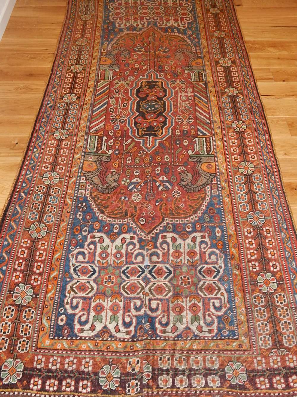 A red ground Qashqai runner, decorated with traditional stylised floral design, fringed.