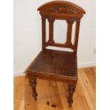 A late Victorian oak hall chair, the carved top rail above fluted supports and a solid seat,