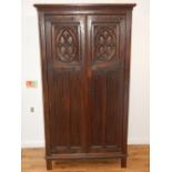 A 1920's Gothic Revival carved oak two door wardrobe on stile feet H.