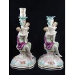 A pair of Meissen style porcelain candlesticks with figural stems on floral scroll bases, H.