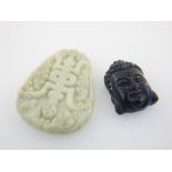 Two Chinese jade pendants; black jade study of Buddha head, H. 3cm, pale green with inscription