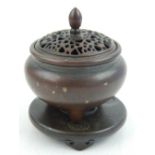 A Chinese bronze circular section cricket box, with pierced lid, on tripod support and circular