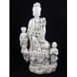 A Chinese blanc de chine figure of Guanyin with two children, seated on a naturalistic base. H.