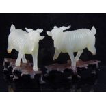 Two Chinese green carvings of herded goats, with hardwood tree form stands. L. 9cm