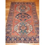 A red ground Kazak carpet, with three geometric medallions to centre, the border blue ground and