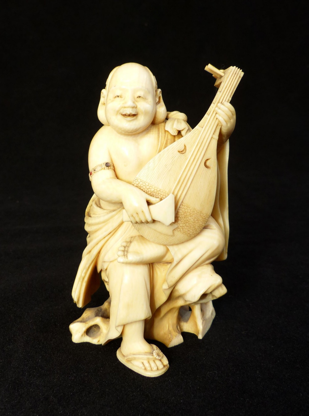 A19th C carved ivory okimono of a plump monk strumming a lute, signed in red seal to base,