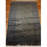 Green ground Turkomen style rug, geometric design within reticulated borders, fringed,