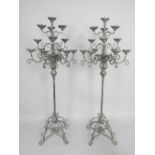 Pair of verdigris metal thirteen sconce floor standing candle holders on scroll bases,