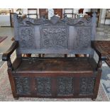 A 1920's carved panelled oak settle with lion and shield top rail over hinged box seat on turned