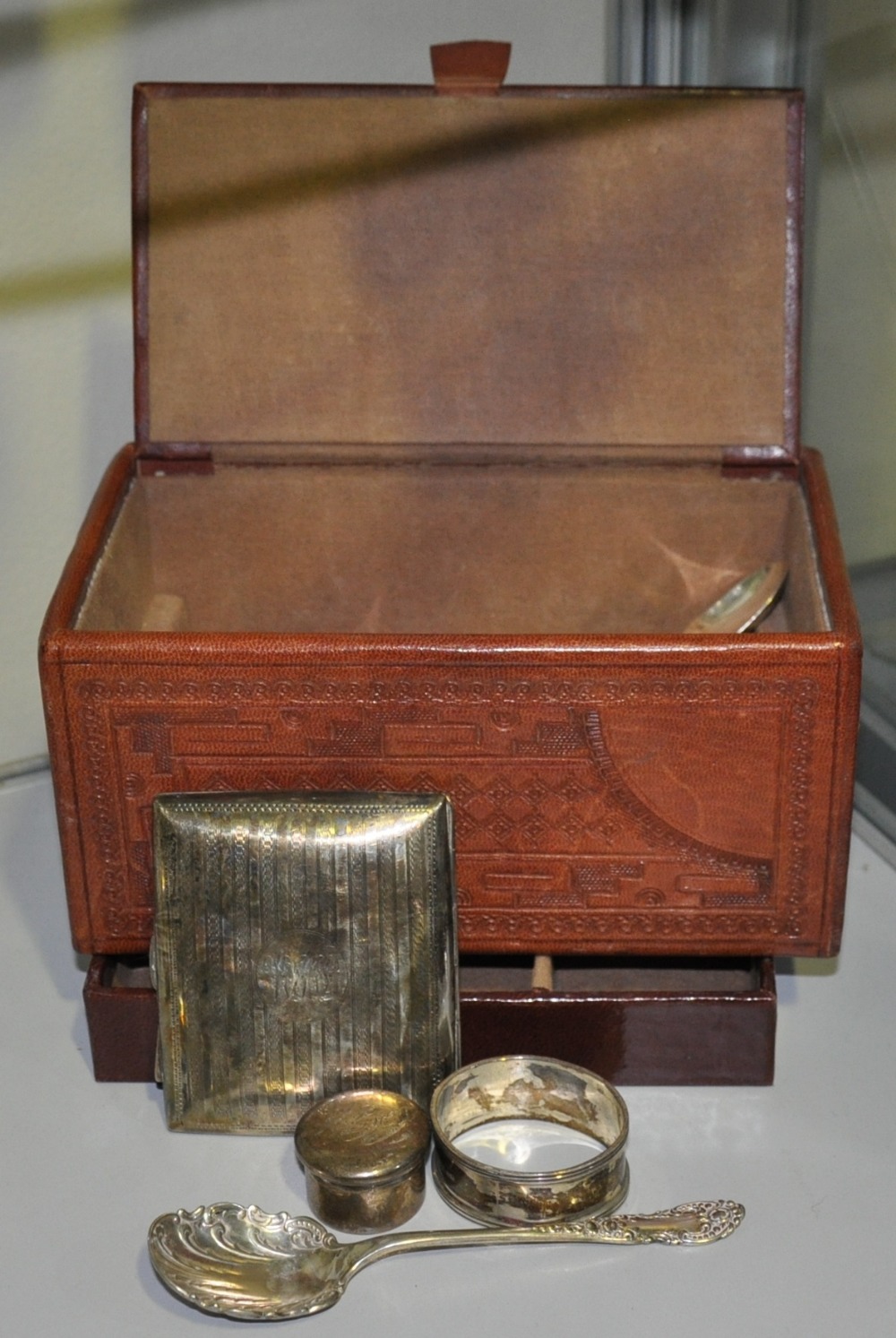 An embossed brown leather jewellery box containing a quantity of Victorian and later small silver