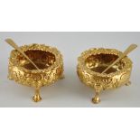 A pair of George III circular silver gilt salts with associated spoons embossed with flowerheads