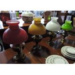 Four vintage brass oil lamps with coloured glass shades