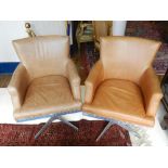 A pair of tan leather and aluminium swivel armchairs, having studded upholstery,