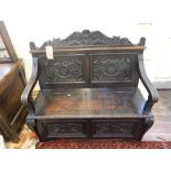 A 17th century style carved oak monks bench, the panelled back above open arms and a box seat, W.