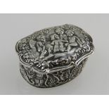 A white metal trinket box, the hinged lid of cartouche form, repousse decorated with cherubs and