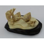 An ivory carving of a dog with two geese and a frog, together with hardwood stand.