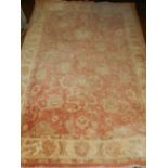 A red ground Ziegler style rug, decorated with scrolling foliage within floral cream borders,