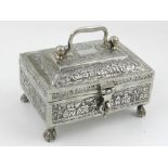 An Indian white metal jewellery box, swing handle to top, repousse embossed with village scene,