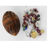 A carved corquila nut, egg form and with a pierced circular design, containing coloured stones,