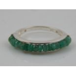 A white metal and emerald dress ring, the rough-cut stones channel set,