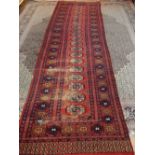 A red ground Bokhara runner, decorated with one row of elephant pad medallions to centre, fringed,