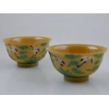 A pair of Chinese yellow ground rice bowls, decorated with cranes flying above stylised green waves,