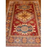 A red ground Kazak rug, having triple pole medallion to centre, multi-bordered and fringed.