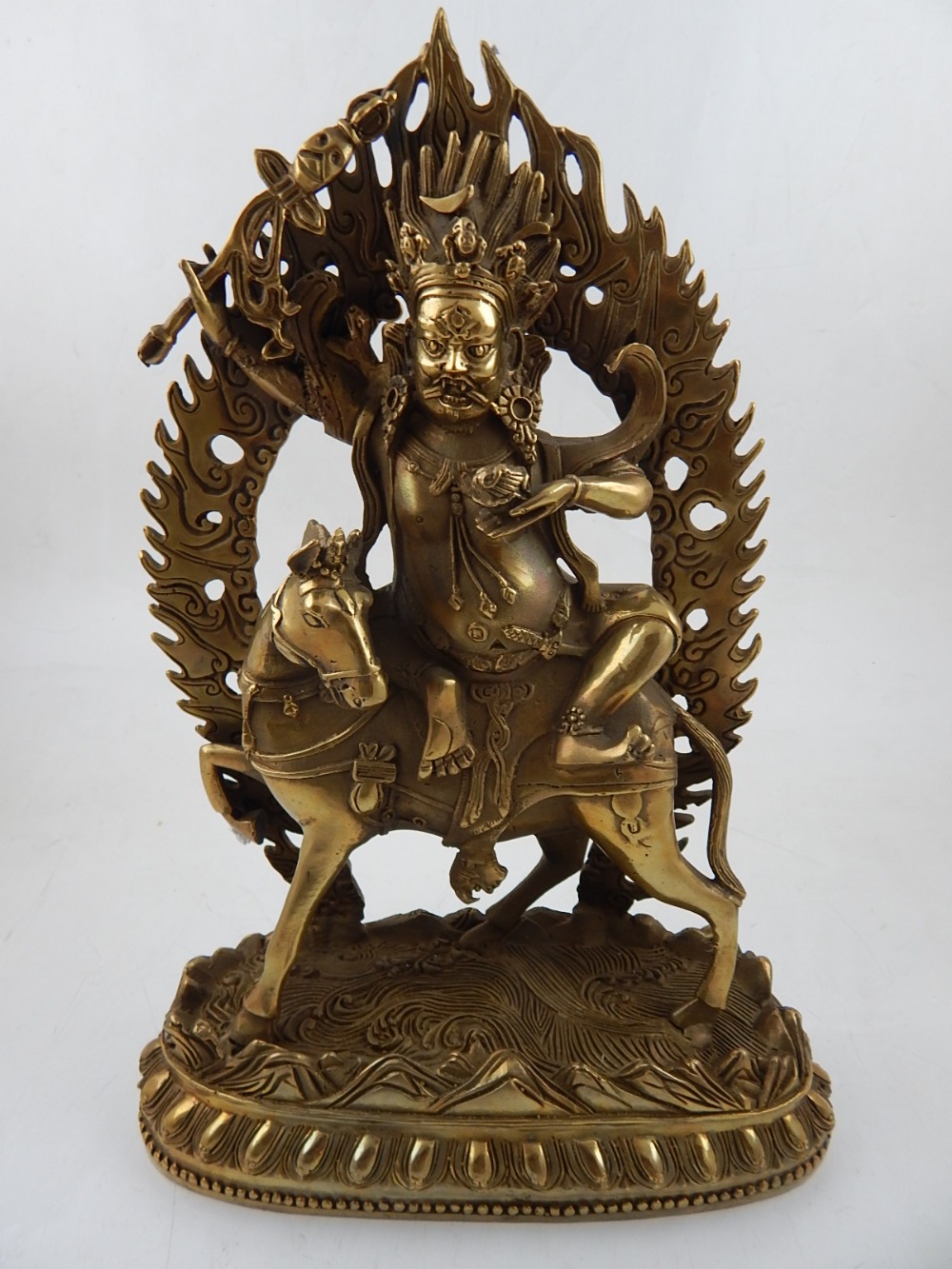 A Tibetan brass figure of a deity, seated on a horse in front of flaming frame, H.