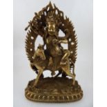 A Tibetan brass figure of a deity, seated on a horse in front of flaming frame, H.