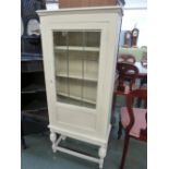 A painted display cabinet with glazed door raised in turned supports,