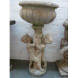 A composite stone planter in the form of a classical urn raised up by two cherubs 90cmH