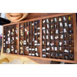 A large collection of thimbles in a wooden display case including Thimble Village, Staffordshire,