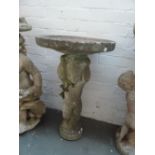 A composite stone bird table held up by a standing cherub 75cmH