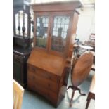 An Arts and Craft oak bookshelf over bureau, glazed doors over three long drawers with carved apron,