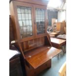 An Arts and Craft oak bookshelf over bureau, glazed doors over three long drawers with carved apron,