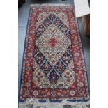 A runner rug with red fields and floral borders and cream fringing 160 x 80cm