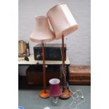 Two standing lamps with turned bases and light pink shades and a bedside lamp