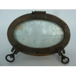 A vintage oval brass ship's porthole with hinged door and catches,