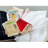 A box of vintage sewing patterns, fabric and linen and lace tablecloths.