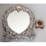 An Edwardian repousse silver strut mirror with a heart shaped bevelled plate within a foliate and