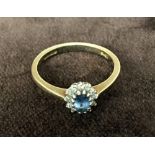 A 9ct gold ring with a pale blue centre stone surrounded with twelve diamond chips