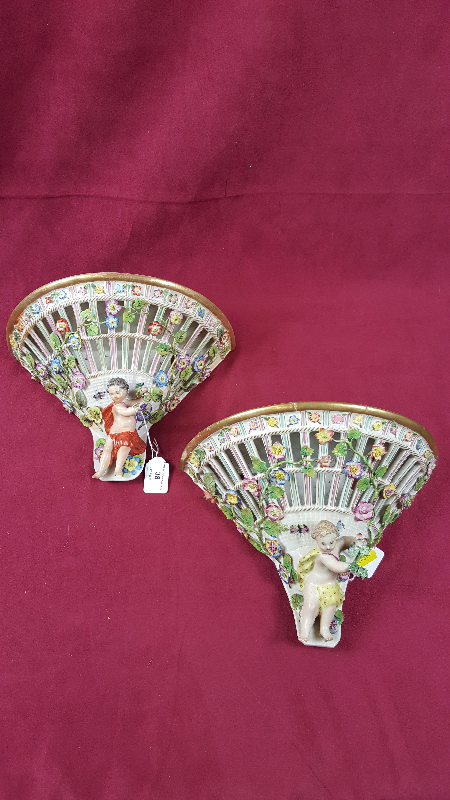 A pair of continental porcelain wall brackets with floral encrusted and cherub decoration