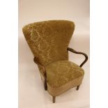 A Danish Art Deco wing back armchair, upholstered in green moquette, raised on rounded tapering