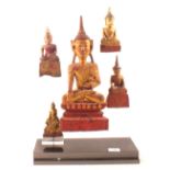 A display of five South East Asian lacquered and giltwood Buddhas on perspex stand
