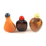 Three Chinese stone snuff bottles, one pale brown with blue stone and gilt metal stopper,